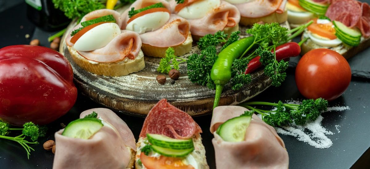 Delicious open-faced sandwiches with ham, eggs, and veggies on a wooden platter.