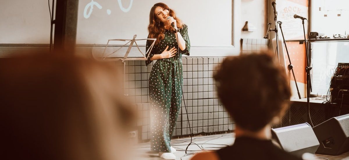 Woman singing passionately on stage at an indoor event with audience engagement.