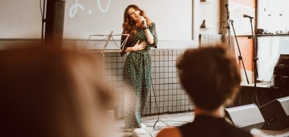 Woman singing passionately on stage at an indoor event with audience engagement.