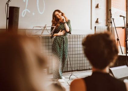 Woman singing passionately on stage at an indoor event with audience engagement.
